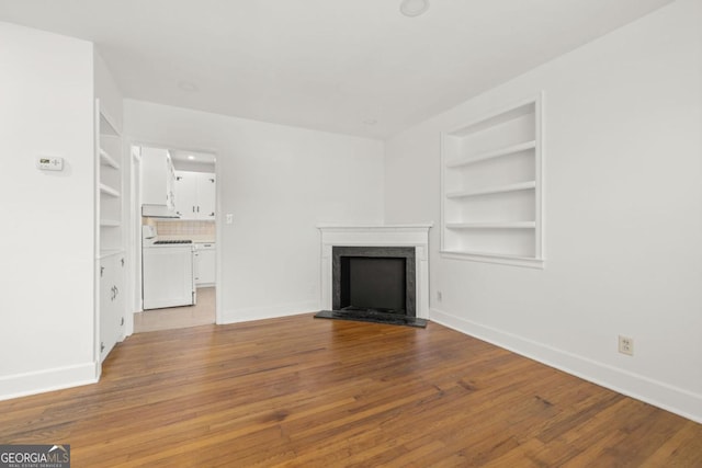 unfurnished living room featuring built in shelves, a premium fireplace, washer / clothes dryer, and light wood-type flooring