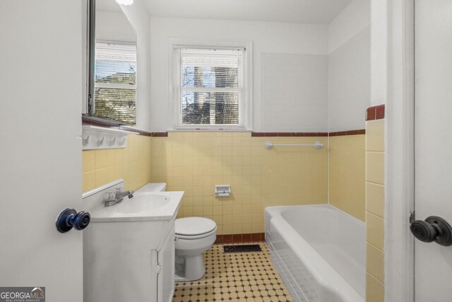 bathroom featuring tile walls, vanity, a bath, and toilet