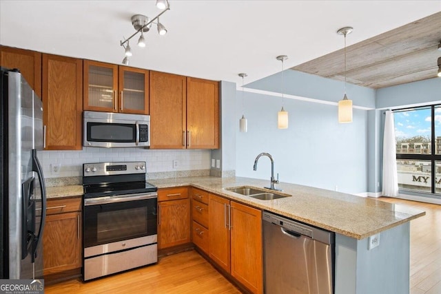 kitchen featuring stainless steel appliances, a peninsula, a sink, and brown cabinets