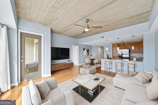 living room featuring light wood finished floors, ceiling fan, visible vents, and baseboards