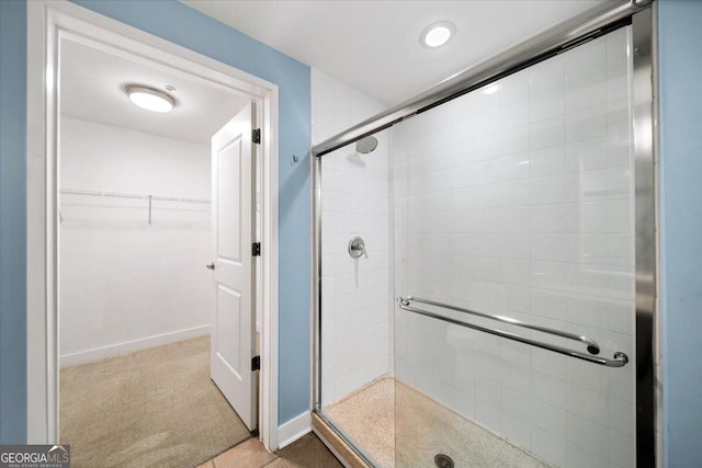 full bath with a spacious closet, a shower stall, and baseboards