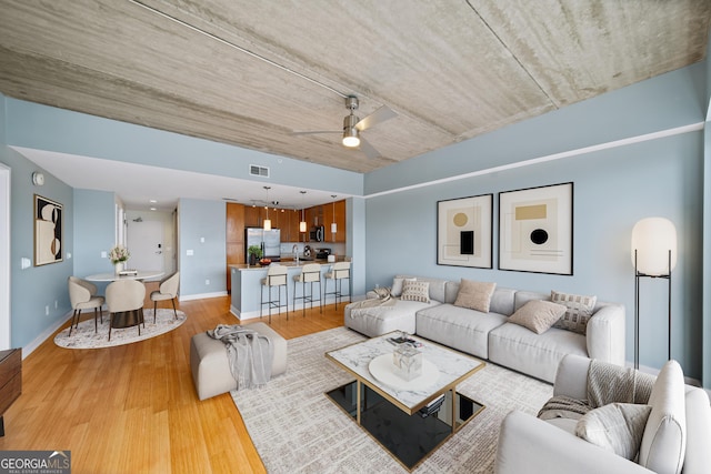 living area featuring light wood-type flooring, ceiling fan, visible vents, and baseboards