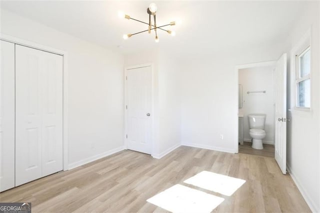 unfurnished bedroom with ensuite bathroom, an inviting chandelier, light wood-type flooring, and a closet