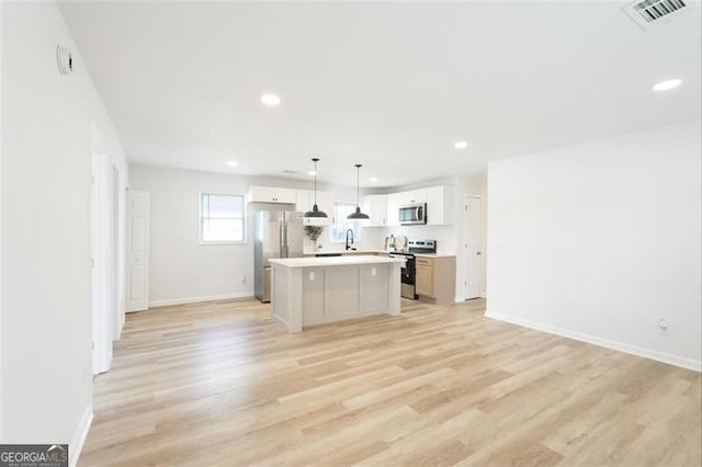 kitchen featuring pendant lighting, appliances with stainless steel finishes, white cabinetry, a kitchen island, and light wood-type flooring