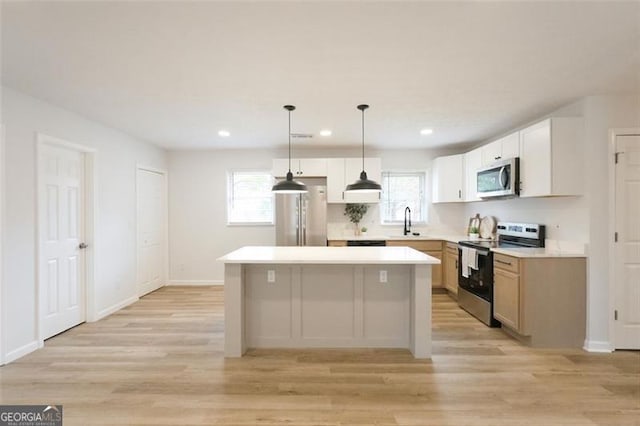 kitchen with sink, appliances with stainless steel finishes, white cabinets, a kitchen island, and decorative light fixtures