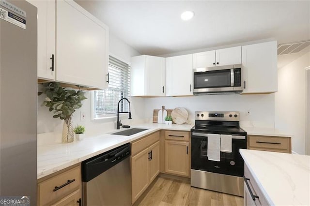 kitchen featuring sink, white cabinets, stainless steel appliances, light stone countertops, and light wood-type flooring