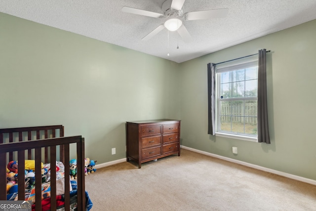 carpeted bedroom with a crib, a textured ceiling, and ceiling fan