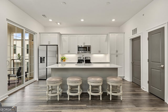 kitchen featuring white cabinetry, stainless steel appliances, a kitchen breakfast bar, and a center island with sink