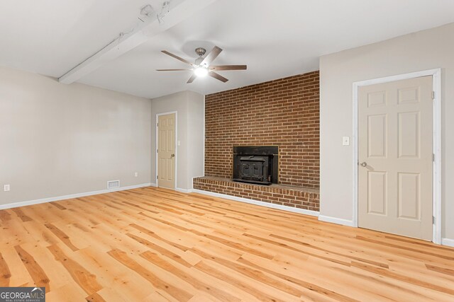 unfurnished living room with hardwood / wood-style flooring, a wood stove, ceiling fan, and beam ceiling