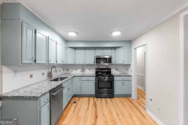 kitchen with sink, light stone counters, light wood-type flooring, ornamental molding, and stainless steel appliances