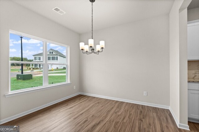 unfurnished dining area with wood-type flooring, plenty of natural light, and a notable chandelier