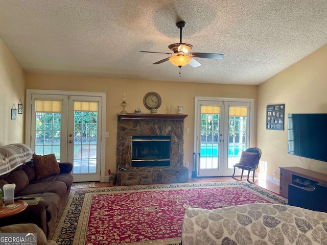 living room with ceiling fan, a fireplace, a textured ceiling, and french doors