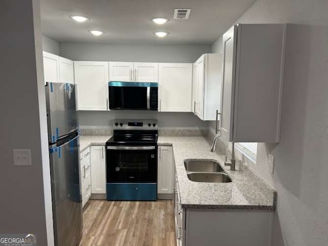 kitchen with sink, white cabinetry, stainless steel appliances, light hardwood / wood-style floors, and light stone countertops