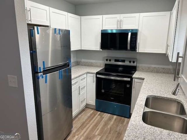 kitchen featuring sink, light stone counters, light wood-type flooring, appliances with stainless steel finishes, and white cabinets