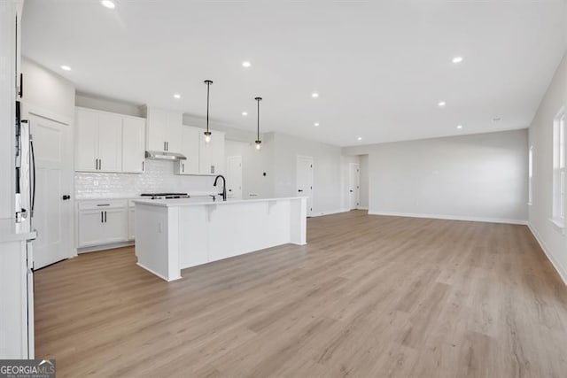 kitchen with white cabinetry, tasteful backsplash, light hardwood / wood-style flooring, a center island with sink, and pendant lighting