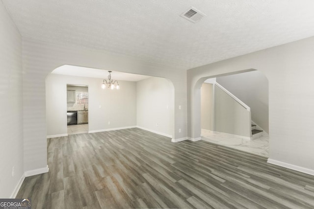 unfurnished living room with a notable chandelier, dark wood-type flooring, and a textured ceiling