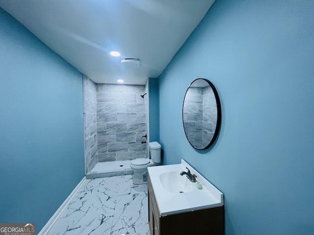 bathroom featuring vanity, a tile shower, and toilet