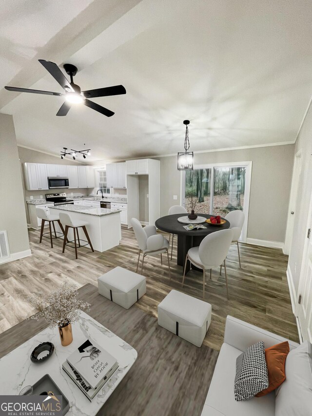 kitchen with sink, appliances with stainless steel finishes, ornamental molding, white cabinets, and a kitchen island