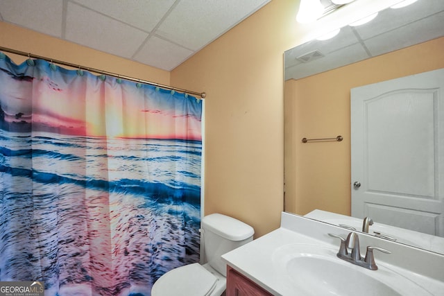 bathroom with walk in shower, vanity, toilet, and a drop ceiling