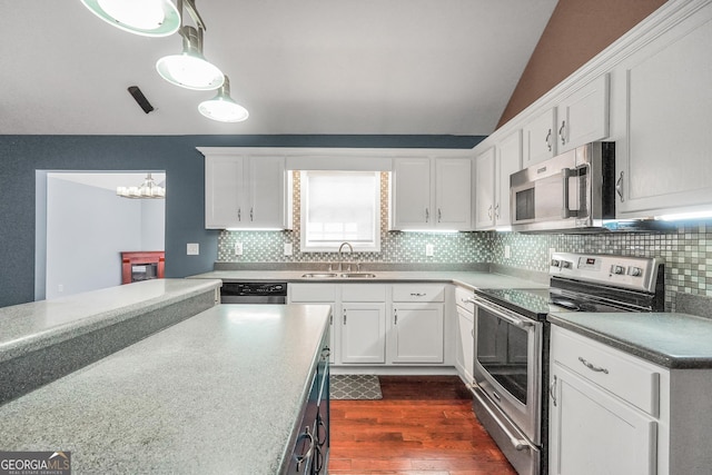 kitchen featuring vaulted ceiling, appliances with stainless steel finishes, sink, white cabinets, and hanging light fixtures