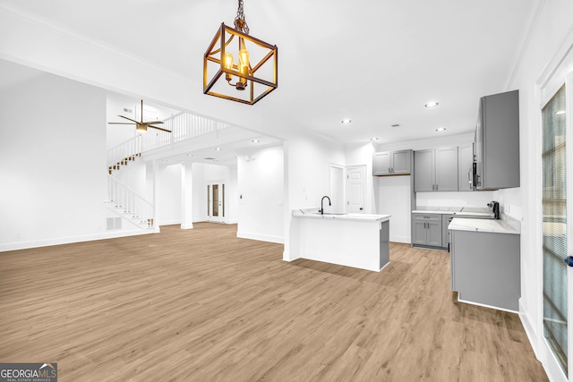 living room featuring crown molding, sink, ceiling fan with notable chandelier, and light wood-type flooring