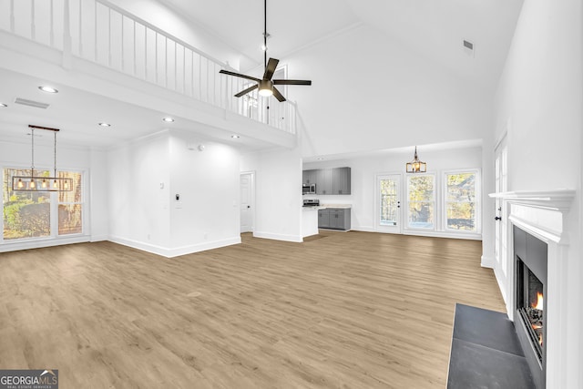 unfurnished living room featuring wood-type flooring, a towering ceiling, and ceiling fan