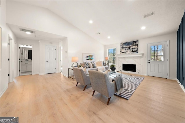 living room with light hardwood / wood-style flooring, a premium fireplace, and vaulted ceiling