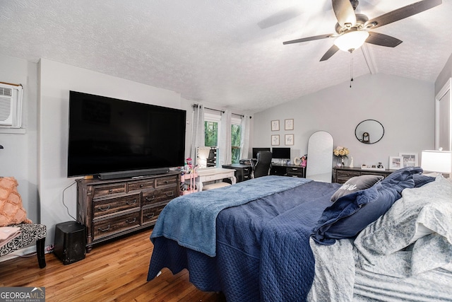 bedroom featuring vaulted ceiling, ceiling fan, light hardwood / wood-style floors, a textured ceiling, and a wall unit AC