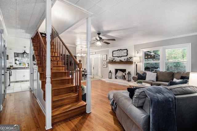 living room with light hardwood / wood-style flooring, crown molding, a fireplace, and ceiling fan with notable chandelier