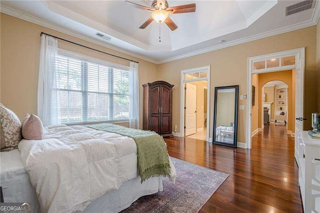 bedroom with dark hardwood / wood-style flooring, crown molding, ceiling fan, and a tray ceiling