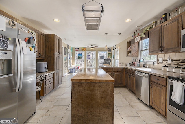 kitchen with light tile patterned flooring, sink, hanging light fixtures, a center island, and stainless steel appliances