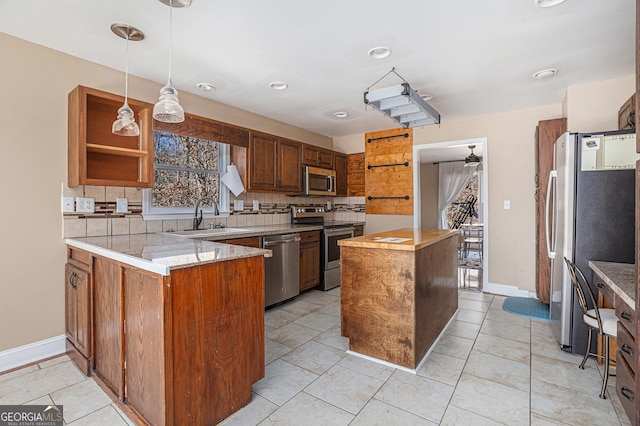 kitchen featuring decorative backsplash, a ceiling fan, appliances with stainless steel finishes, a sink, and a center island