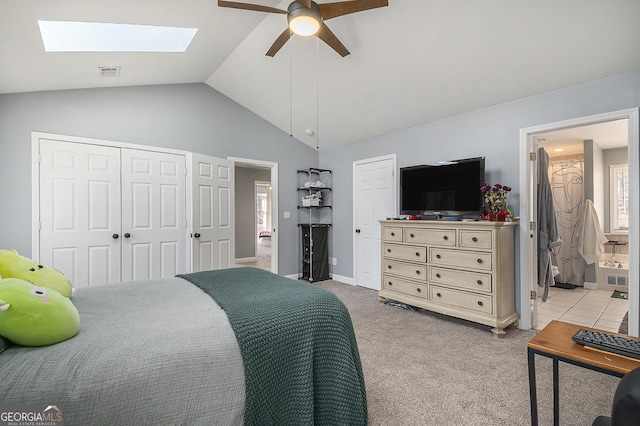 carpeted bedroom with ensuite bathroom, vaulted ceiling with skylight, and ceiling fan