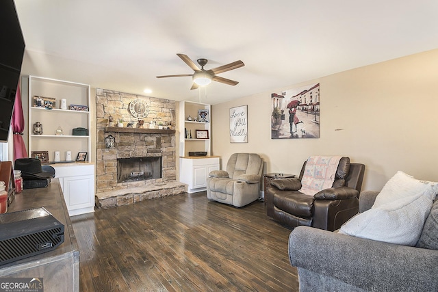 living room with a stone fireplace, dark wood-type flooring, built in features, and ceiling fan