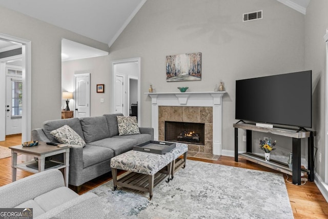 living room with crown molding, a tiled fireplace, high vaulted ceiling, and hardwood / wood-style flooring