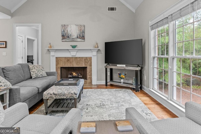 living room featuring hardwood / wood-style flooring, crown molding, vaulted ceiling, and a tile fireplace