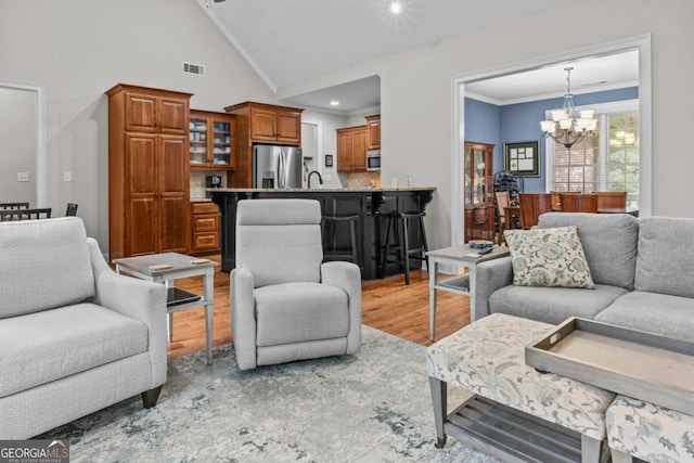 living room with an inviting chandelier, high vaulted ceiling, sink, ornamental molding, and light wood-type flooring