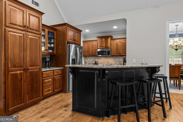 kitchen featuring a kitchen bar, light stone counters, appliances with stainless steel finishes, a notable chandelier, and backsplash