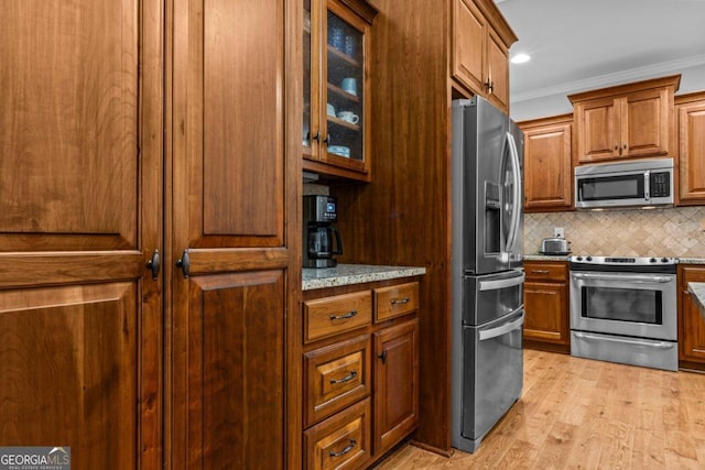 kitchen with crown molding, light hardwood / wood-style flooring, appliances with stainless steel finishes, tasteful backsplash, and light stone countertops