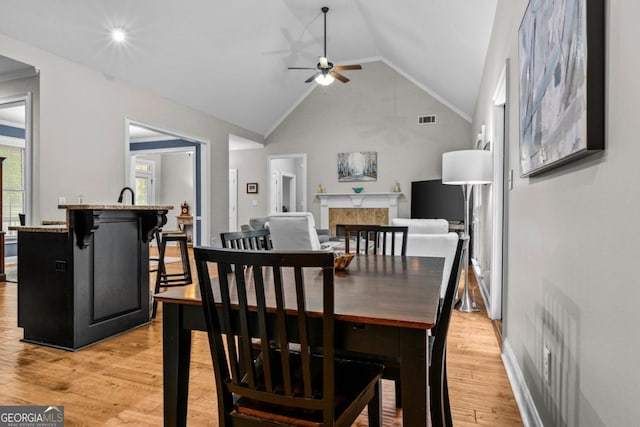 dining space with vaulted ceiling, a tile fireplace, light hardwood / wood-style floors, and ceiling fan