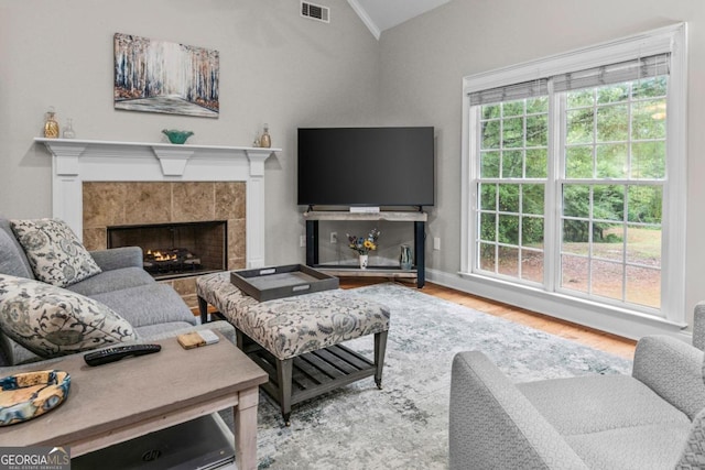 living room featuring a tiled fireplace, vaulted ceiling, hardwood / wood-style floors, and crown molding