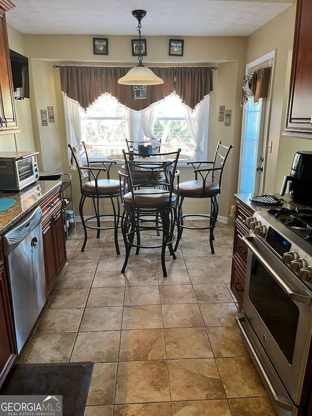 kitchen with tile patterned floors, appliances with stainless steel finishes, decorative light fixtures, and dark stone counters