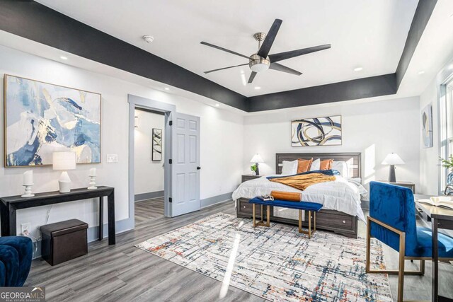 bedroom with hardwood / wood-style flooring, a raised ceiling, and ceiling fan