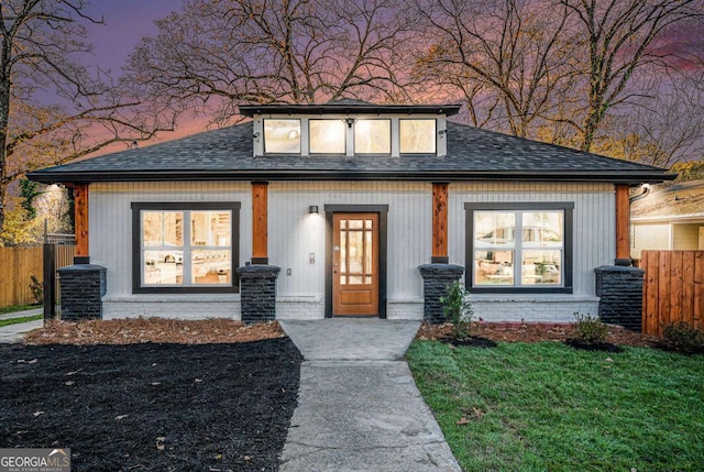 view of front of house featuring brick siding, fence, a lawn, and roof with shingles