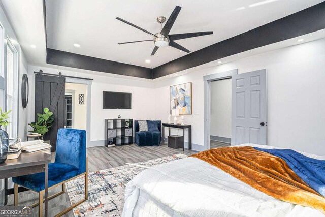 bedroom with hardwood / wood-style flooring, a barn door, and ceiling fan