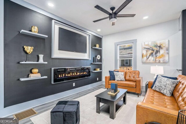 living room featuring built in shelves, ceiling fan, and light wood-type flooring