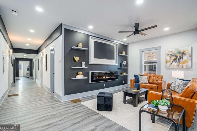 living room with built in shelves, ceiling fan, and light wood-type flooring