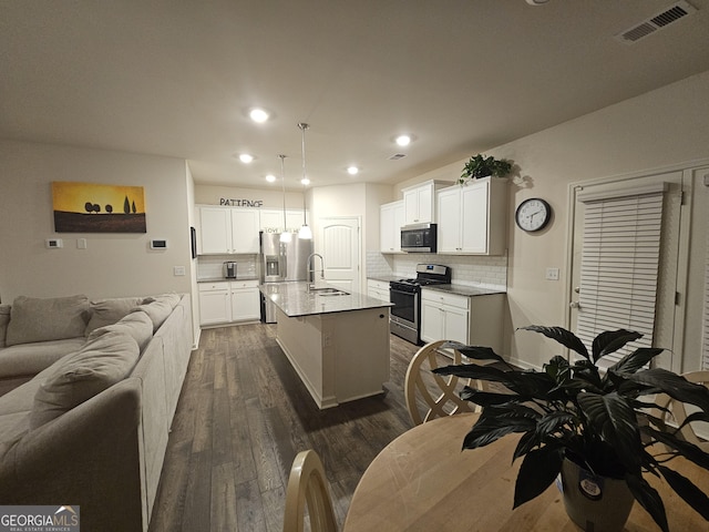 kitchen with appliances with stainless steel finishes, decorative light fixtures, sink, a kitchen island with sink, and light stone counters