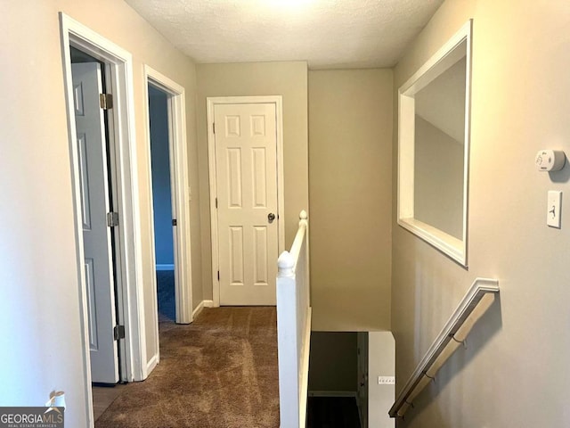 hallway featuring dark colored carpet and a textured ceiling