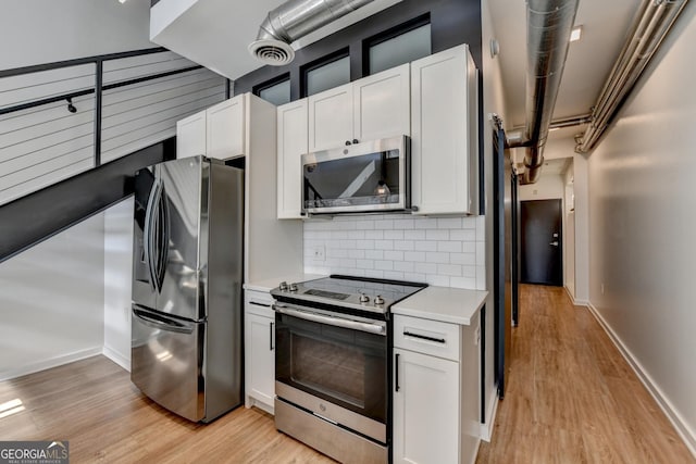 kitchen with stainless steel appliances, white cabinetry, tasteful backsplash, and light wood-type flooring